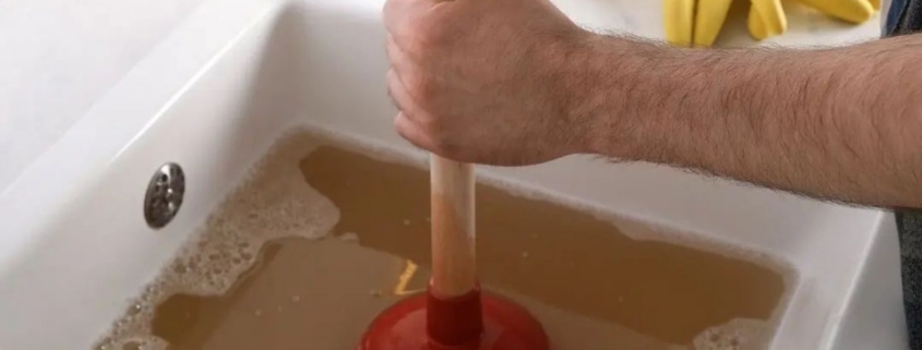 Plumber inspecting a clogged household drain to identify buildup, debris, and plumbing issues causing recurring drain clogs in the home | Causes of Recurring Drain Clogs in Your Home