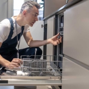 Troubleshooting Dishwasher Plumbing Issues A technician kneels to inspect an open kitchen dishwasher while troubleshooting potential underlying plumbing and drainage problems for repair.