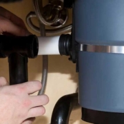 Repairing Leaking Garbage Disposal Hands work under a kitchen sink to inspect and repair plastic pipe connections causing a garbage disposal unit to leak.
