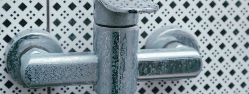 A chrome bathroom faucet showing heavy white mineral residue buildup and stains caused by hard water exposure over time.